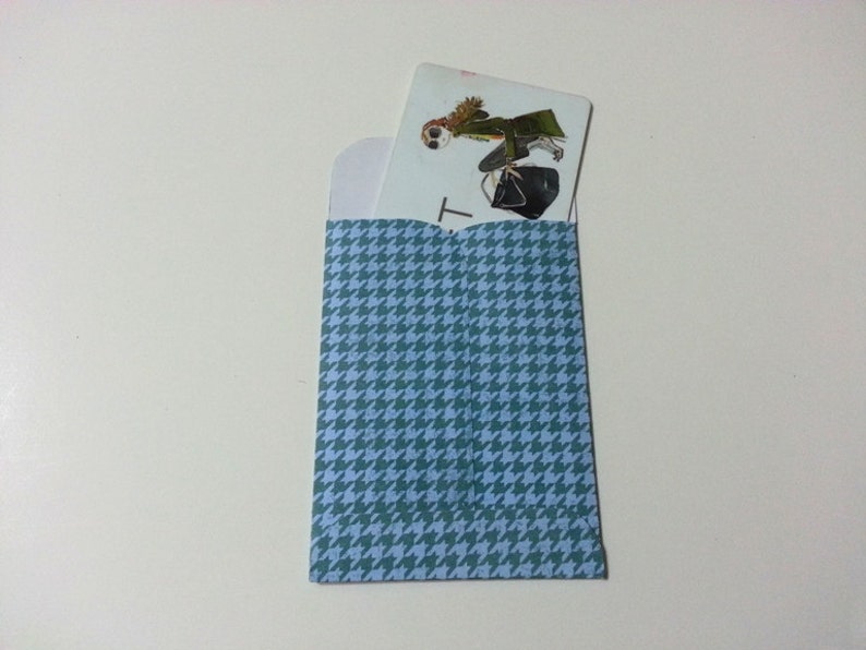 May include: A blue and white patterned envelope with a white card inside. The card has a drawing of a person wearing a green coat and a hat. The card has the letter "T" printed on it.