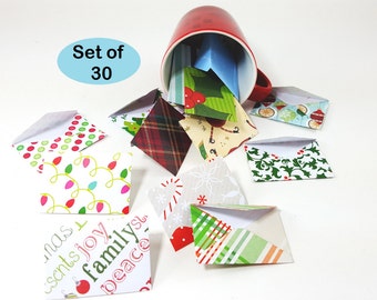 May include: A red mug tipped over, spilling out a set of 30 small, folded paper envelopes. The envelopes feature various festive patterns, including Christmas lights, plaid, and holiday-themed text. The text "Set of 30" is in a blue oval.