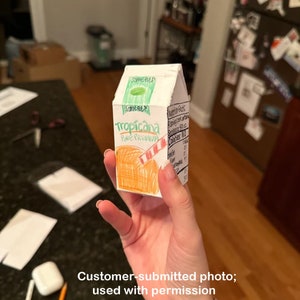 Puede incluir: Una caja de cart&oacute;n de zumo de naranja Tropicana Pure Premium dibujada a mano. La caja es naranja y blanca con las palabras "Tropicana Pure Premium" escritas en marcador negro. La caja tambi&eacute;n tiene una pajita a rayas rojas y blancas dibujada en ella. La caja est&aacute; etiquetada como "Some Pulp" y tiene una etiqueta de informaci&oacute;n nutricional.