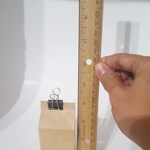 Puede incluir: Una bolsa de papel marr&oacute;n con una grapa negra que mantiene la parte superior cerrada. La bolsa mide 15 cm de alto y est&aacute; al lado de una regla de madera.