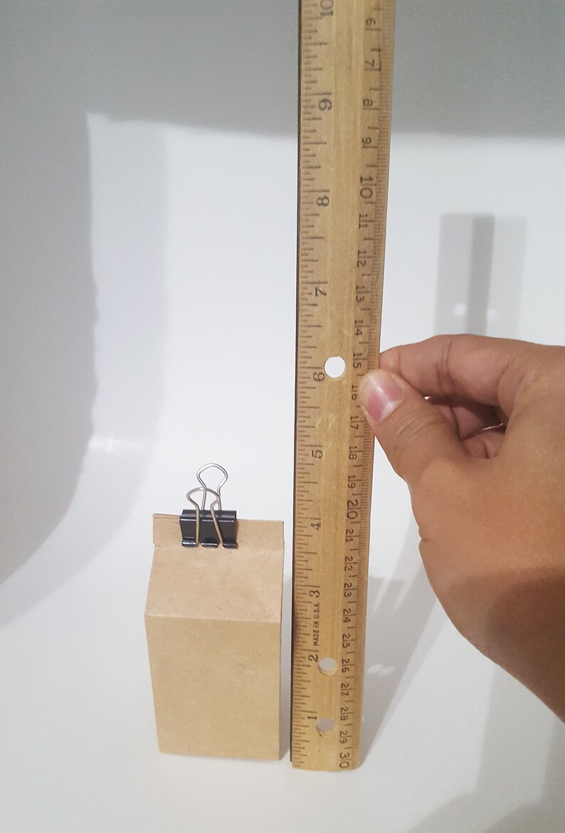 Puede incluir: Una bolsa de papel marr&oacute;n con una grapa negra que mantiene la parte superior cerrada. La bolsa mide 15 cm de alto y est&aacute; al lado de una regla de madera.
