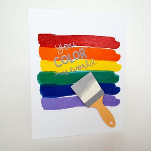May include: A white card with a rainbow of colored stripes and the text "you color my world" in silver lettering. A small paintbrush is on the card.