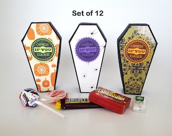 May include: Three coffin-shaped boxes with black edges and decorative fronts featuring pumpkins, spiders, and damask patterns. Each box has a circular label reading OPEN IF YOU DARE. Included are a lollipop, a Hershey's bar, Chewy Lemonhead, and Tic Tacs.