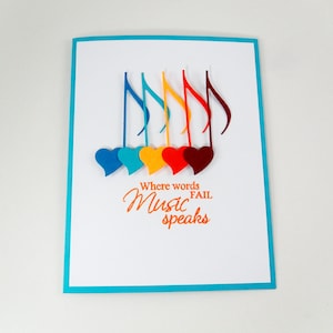 May include: A white card with a turquoise border features a colorful design of musical notes and hearts. The text "Where words fail Music speaks" is printed in orange.