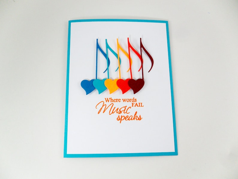 May include: A white card with a turquoise border features a colorful design of musical notes and hearts. The text "Where words fail Music speaks" is printed in orange.