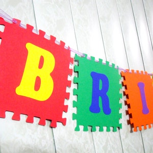 May include: A colorful felt banner spelling out the name "BRIAN" in bright colors. Each letter is on a separate piece of felt with a zig-zag edge. The letters are red, green, orange, yellow, and purple.