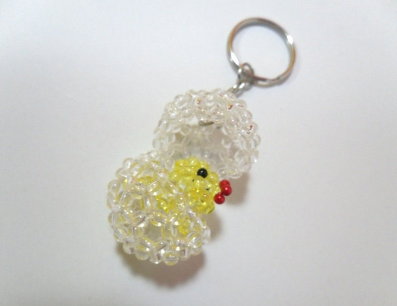 May include: A yellow beaded chick hatching from a clear beaded egg with a silver key chain attached.