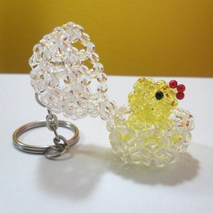 May include: A yellow beaded chick keychain with red and black bead accents, sitting inside a clear beaded egg with a silver key ring.
