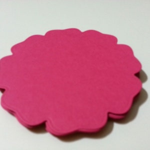 Pode incluir: Uma pilha de formas de flores de papel rosa com bordas festoneadas.