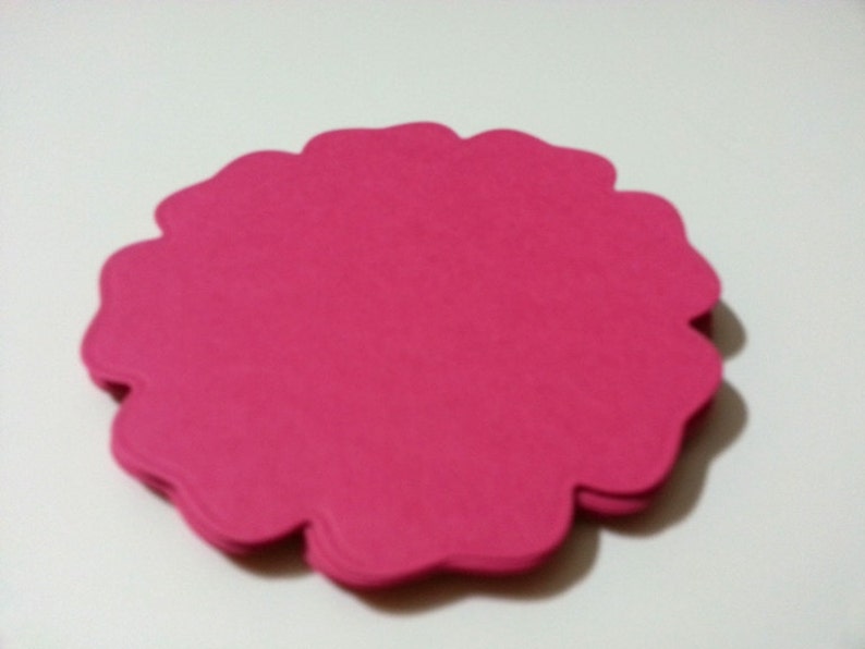 Pode incluir: Uma pilha de formas de flores de papel rosa com bordas festoneadas.