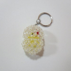 May include: A yellow beaded keychain with a clear plastic covering. The keychain is shaped like a chick with red eyes and a yellow beak.