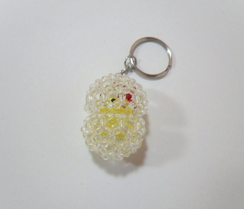 May include: A yellow beaded keychain with a clear plastic covering. The keychain is shaped like a chick with red eyes and a yellow beak.