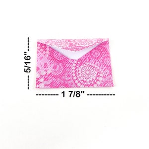 May include: A small, folded envelope with a pink floral pattern. The envelope measures 1 7/8 inches wide and 5/16 inches high. The design features a white floral pattern on a pink background.