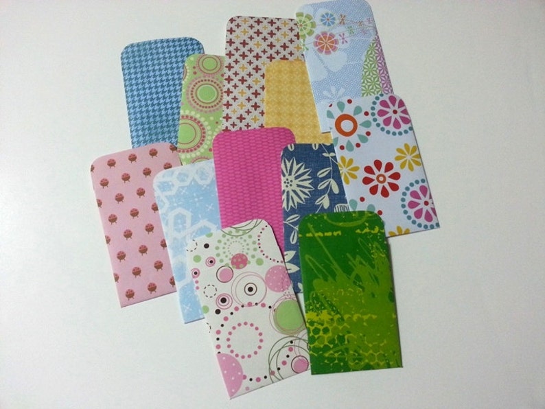 May include: A set of 12 colorful patterned envelopes with rounded corners. The envelopes are made of paper and have a variety of designs, including floral, geometric, and abstract patterns.