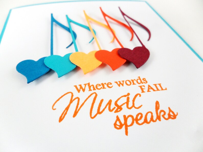 May include: A white card with the text "Where words fail Music speaks" in orange lettering.  There are six colorful musical notes with hearts attached to the bottom of each note.