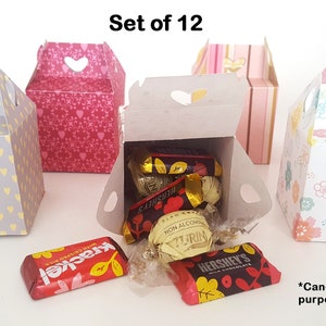 Könnte beinhalten: Set aus 12 dekorativen Geschenkboxen mit verschiedenen Mustern, darunter Herzen, Streifen und Blumen. Jede Box hat einen herzförmigen Ausschnitt und einen Griff. Die Boxen werden mit Süßigkeiten zur Präsentation gezeigt.