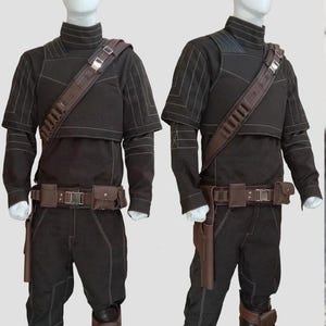 May include: Two black costumes displayed on mannequins. Each costume includes a high-collared top, pants, a brown belt with pouches, and a shoulder strap. The outfits have white stitching details and brown accents, with a holster and knee pads.