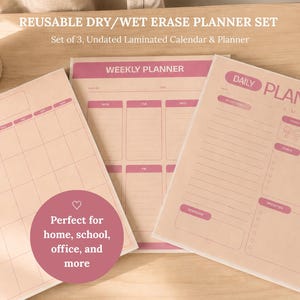 May include: A set of three reusable dry or wet erase planners in light pink with dark pink text and lines. The set includes a monthly calendar, a weekly planner, and a daily planner sheet. Each sheet features organized sections for scheduling.