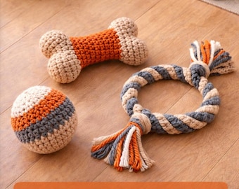 May include: Crocheted pet toys in a variety of shapes and colors. The image features a bone-shaped toy, a ball, and a rope toy. The toys are in shades of orange, gray, and beige. The image also includes text that says "Crochet Pet Toy Pattern".
