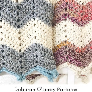 May include: Two crocheted baby blankets, one in white, gray, and blue, and the other in white, pink, and purple. The blankets are folded and placed on a white surface. The text "Breckenridge Baby Blanket" is at the top of the image. The text "Deborah O'Leary Patterns" is at the bottom of the image.