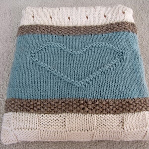May include: A knitted throw blanket with a blue, brown, and white striped pattern. The center of the blanket features a heart-shaped design.