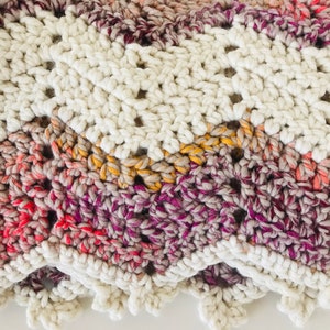 May include: A crocheted blanket with a white border and a multi-colored center. The center is made of a gradient yarn in shades of pink, orange, yellow, and purple.