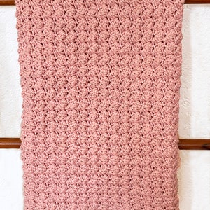 May include: A soft, pink crocheted baby blanket with a textured stitch pattern.