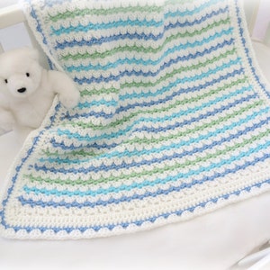 May include: A white crocheted baby blanket with blue, green, and white stripes. The blanket has a scalloped edge.