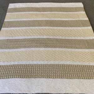 May include: A knitted throw blanket with alternating stripes of beige and white.