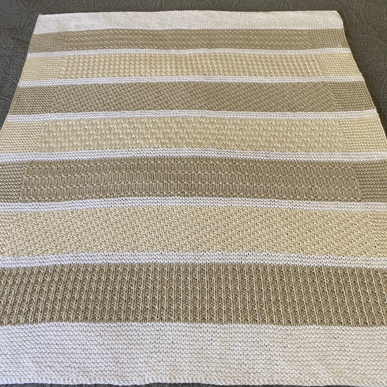 May include: A knitted throw blanket with alternating stripes of beige and white.