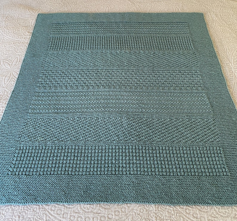 May include: A teal blue knitted blanket with a textured pattern. The blanket is made with a variety of stitches, creating a unique and interesting design.