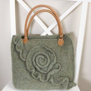 May include: A green knitted tote bag with a large, three-dimensional flower design and brown leather handles.
