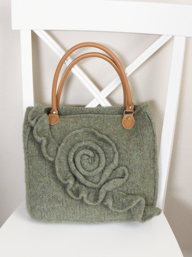 May include: A green knitted tote bag with a large, three-dimensional flower design and brown leather handles.