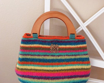 May include: A striped crocheted handbag with a wooden handle. The bag is made with a variety of colors, including orange, blue, green, and pink. The bag has a small decorative embellishment on the front.