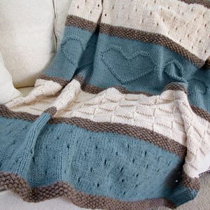 May include: A knitted throw blanket with stripes of brown, cream, and blue. The blanket features a heart pattern in the blue stripes.
