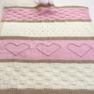 May include: A pink and white knitted baby blanket with a brown stripe and a white teddy bear peeking out from the top.