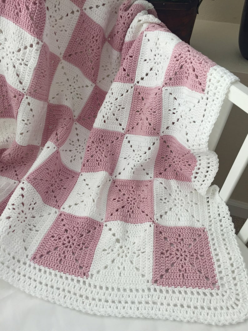May include: A pink and white crocheted baby blanket with a checkered pattern. The blanket is made with a delicate, lacy stitch.