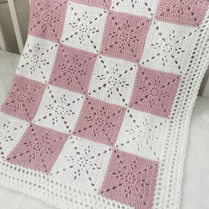 May include: A pink and white crocheted baby blanket with a square pattern. The blanket has a white border.
