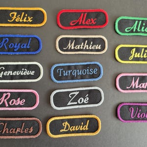 Peut inclure: Collection de patchs nominatifs brodés de différentes couleurs. Chaque patch présente un nom en écriture cursive, avec une bordure contrastante. Les noms incluent Félix, Alex, Alice, Royal, Mathieu, Julia, Geneviève, Turquoise, Maria, Rose, Zoé, Charles, David et Violet.
