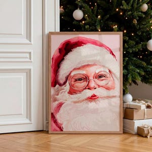 Puede incluir: Pintura en acuarela enmarcada de Papá Noel. La obra presenta el rostro de Papá Noel, con un gorro rojo y mejillas rosadas. Lleva gafas redondas y tiene una larga barba blanca. El marco es de color madera clara.