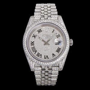 May include: A luxury wristwatch with a silver face and band, fully encrusted with sparkling gemstones. The watch face features black Roman numerals and a date display at the 3 o'clock position. The watch is set against a black background.