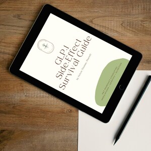 May include: A black tablet displaying the title "GLP-1 Side-Effect Survival Guide" with a green and white design. A black pencil and a blank white paper are next to the tablet on a wooden surface.