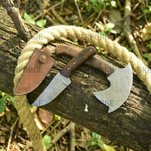 May include: A collection of handcrafted knives and a small axe with wooden handles and patterned blades. A brown leather sheath is included. The items are displayed on a weathered log with a rope.