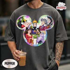 A person wearing a gray t-shirt with a colorful graphic of Disney characters, including a group of women and a character with a crown. The person is holding a drink in their hand.
