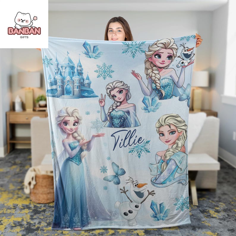 A woman is holding up a blanket featuring illustrations of characters from the Disney movie Frozen, including Elsa, Olaf, and other beloved characters.