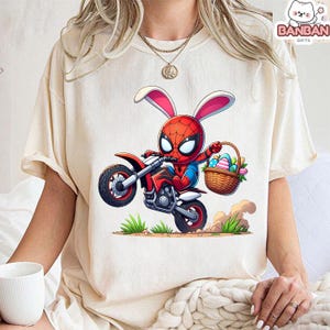 A person wearing a white t-shirt with a graphic of Spider-Man riding a motorcycle and holding a basket of Easter eggs.