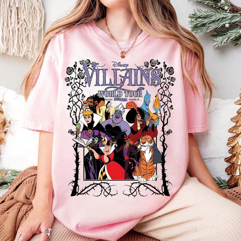A person wearing a pink t-shirt with a graphic design featuring characters from the Disney animated film "The Villains: World Tour".