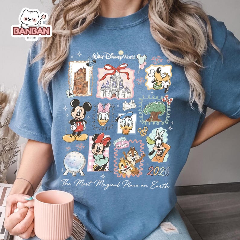 A person wearing a blue t-shirt with various Disney characters and a Disney World logo, holding a pink mug.