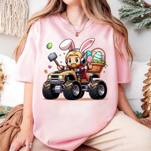 A person wearing a pink t-shirt with a cartoon image of a bunny riding a monster truck.