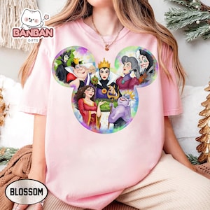 A person wearing a pink t-shirt with a colorful graphic of Disney villain characters from the Disney animated film series.
